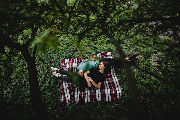 Foto gratuita niña con su novio se encuentran en una tela escocesa en el parque