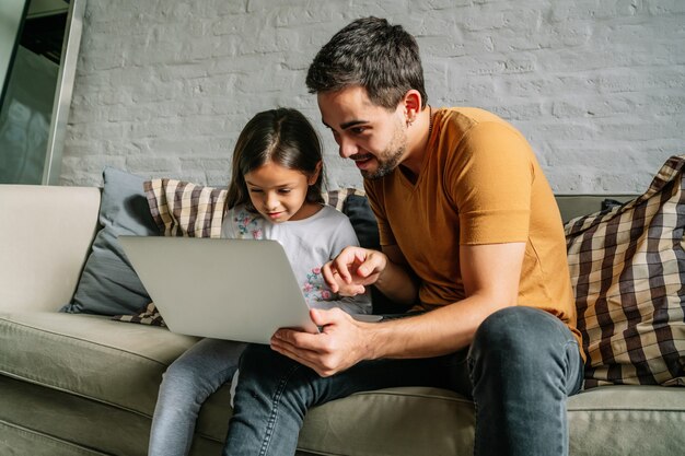 Niña y su padre usando una computadora portátil juntos en casa.