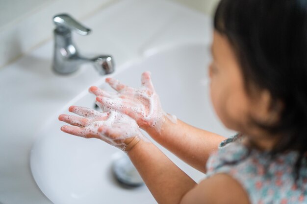 Una niña del sudeste asiático se lava las manos en el baño para prevenir virus y gérmenes