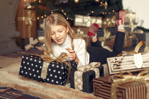 Niña en un suéter blanco cerca del árbol de navidad con presente