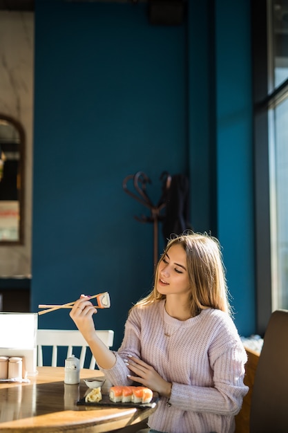 Niña de suéter blanco comiendo sushi para el almuerzo en un pequeño caffe