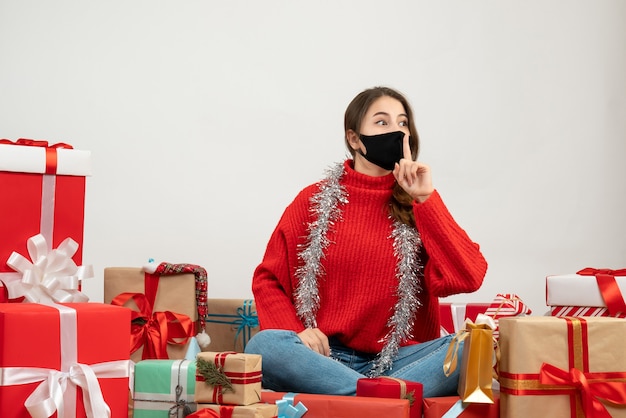 Niña con suéter rojo haciendo shh firmar sentados alrededor de regalos en blanco