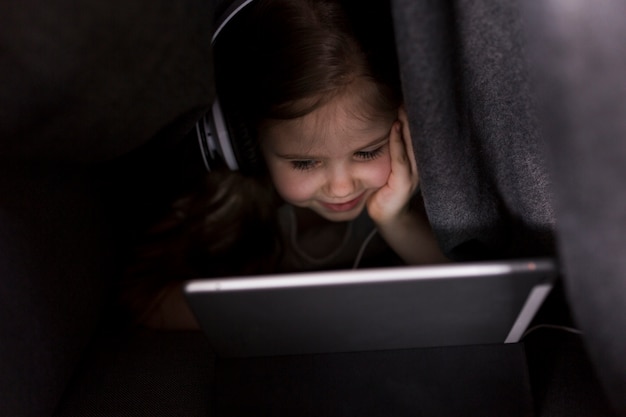 Niña con tablet debajo de mantel