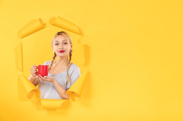 Niña con taza de té sobre fondo de papel amarillo rasgado publicidad facial compras