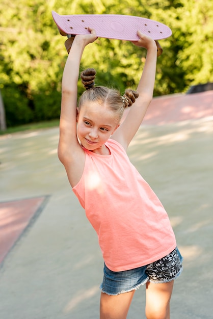 Foto gratuita niña, tenencia, patineta, encima de la cabeza