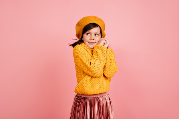 Niña tímida posando en la pared rosa. niño lindo en traje amarillo.