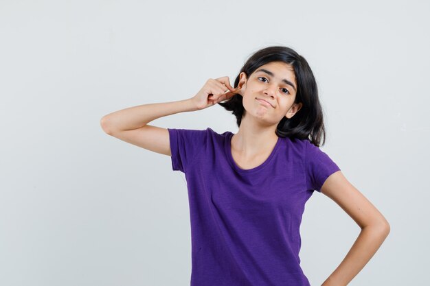 Niña tirando hacia abajo el lóbulo de la oreja en camiseta y mirando confundido