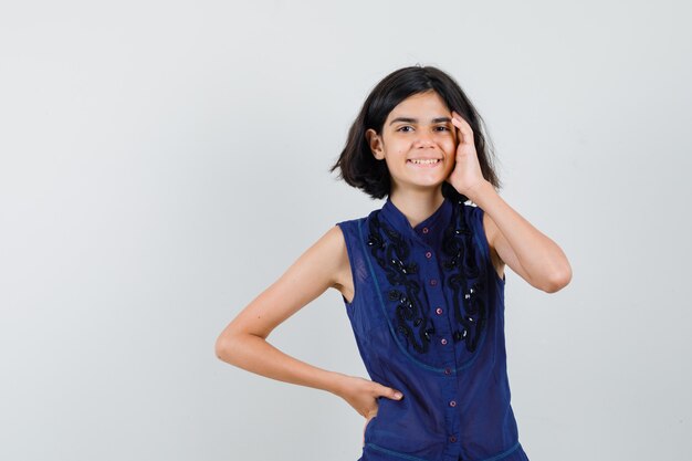 Niña tocando la cara con la mano en la blusa azul y mirando avergonzado