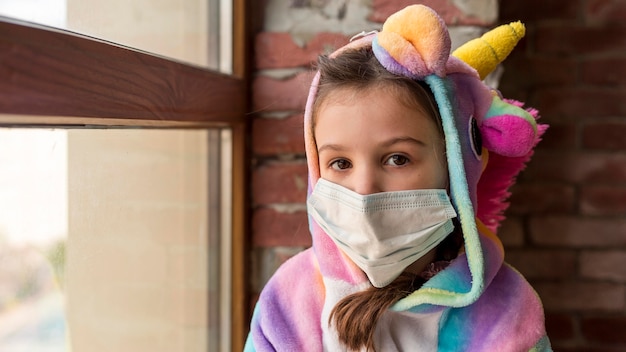 Foto gratuita niña en traje de dinosaurio en casa con mascarilla durante la cuarentena