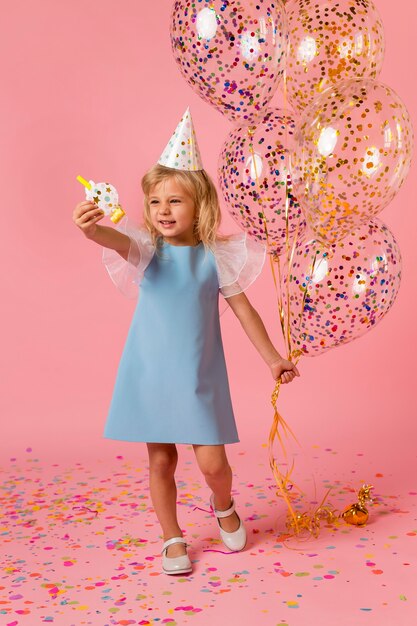 Niña en traje con globos y gorro de fiesta