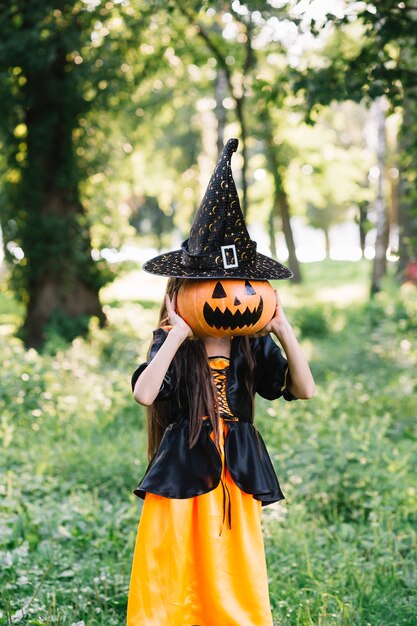 Niña en traje de hechicera cerrando la cara por calabaza