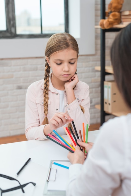 La niña triste que elige los lápices coloreados se sostiene por el psicólogo de sexo femenino