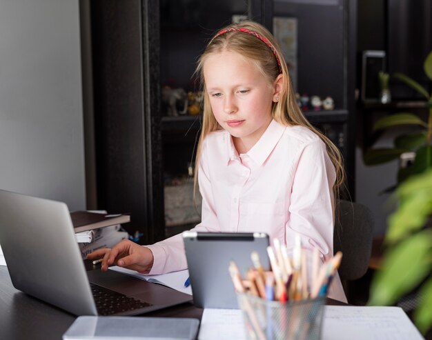 Niña usando su computadora portátil y una tableta para clases en línea