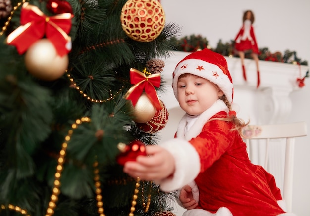 Niña vestida de papa noel decorando el árbol de navidad
