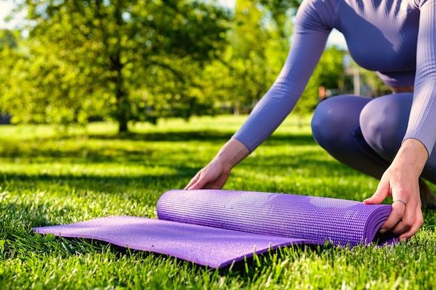 Niña vestida con ropa de yoga sosteniendo su alfombra de yoga ecológica en la hierba verde del parque