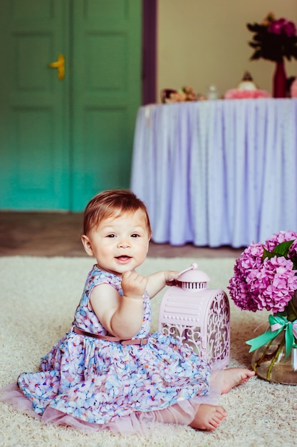 Niña en vestido con flores se sienta en la alfombra con linterna de color rosa en el brazo