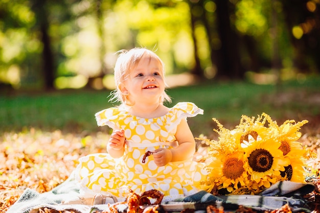 La niña en vestido manchado amarillo se sienta en la manta en el parque