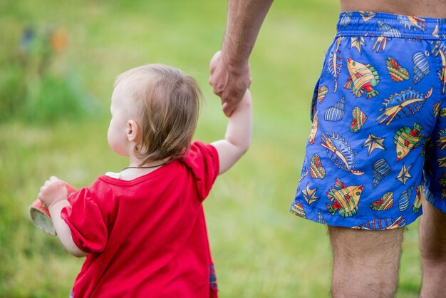 Niña en vestido rojo camina por el campo con la mano del padre