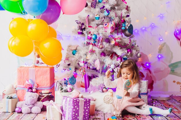 Niña en vestido rosa juega en la habitación con el árbol de Navidad rosa