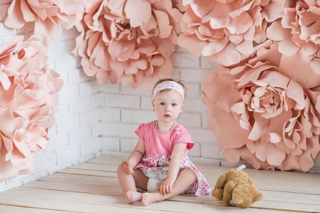 Niña en vestido rosa se sienta entre grandes flores de papel rosa