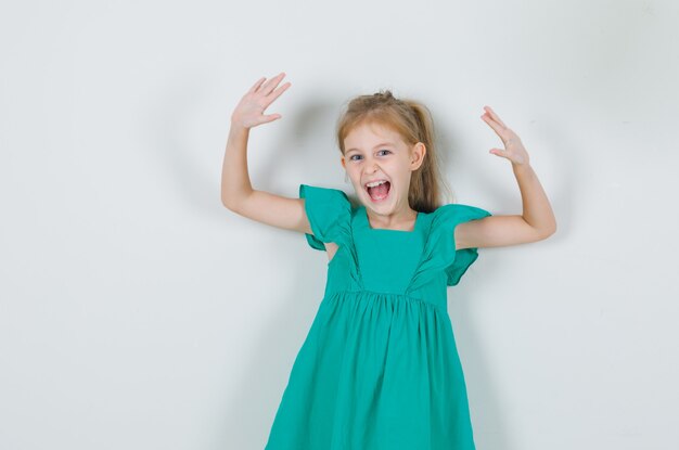 Niña en vestido verde levantando las manos y gritando y mirando enérgico