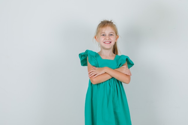 Niña en vestido verde de pie con los brazos cruzados y mirando alegre