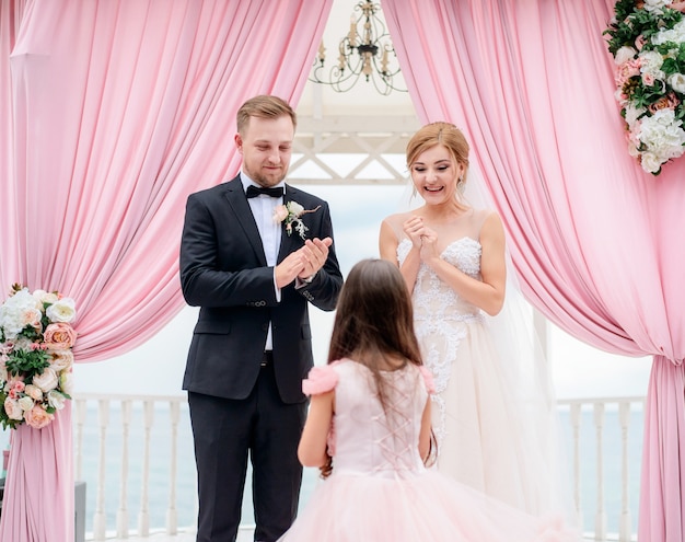 Niña viene a la novia y el novio con anillos de boda durante la ceremonia