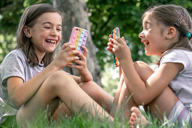 Las niñas al aire libre con teléfonos en un estuche con granos revientan, un moderno juguete antiestrés.