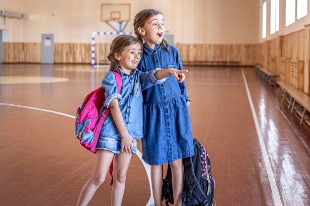 Niñas colegialas de primaria con mochilas después de la escuela en el gimnasio de la escuela