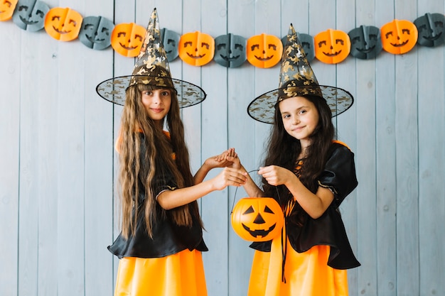 Niñas en disfraces de Halloween con cubo de calabaza