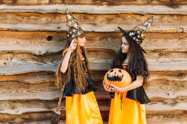 Niñas en disfraces de Halloween con escoba y calabaza mirándose