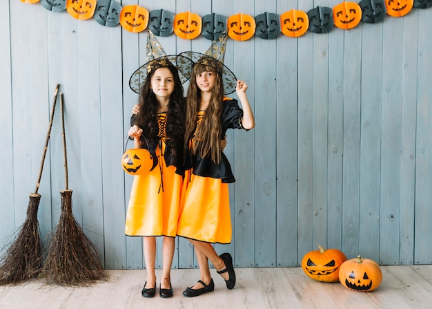 Niñas en disfraces de Halloween con sombreros puntiagudos de pie abrazando