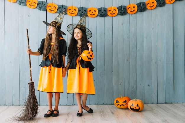 Niñas en disfraces de Halloween tomados de la mano y mirando a otro lado