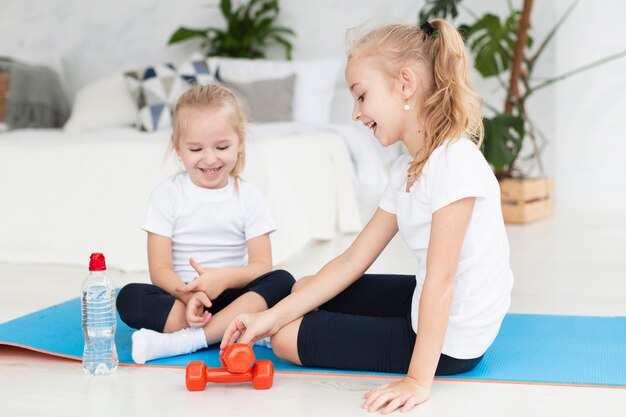 Niñas felices haciendo ejercicio en casa en estera de yoga con pesas