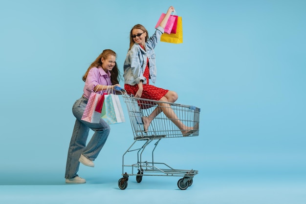 Niñas felices y sonrientes con muchas bolsas de compras divirtiéndose aisladas sobre el fondo azul del estudio