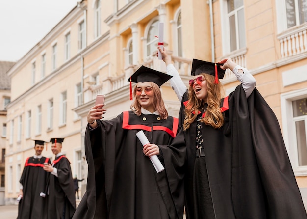 Niñas felices tomando selfie con diploma