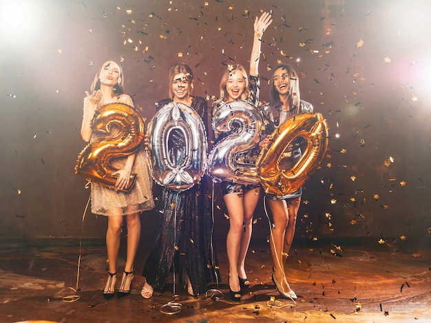 Niñas hermosas felices en elegantes vestidos de fiesta sexy con globos dorados y plateados 2020