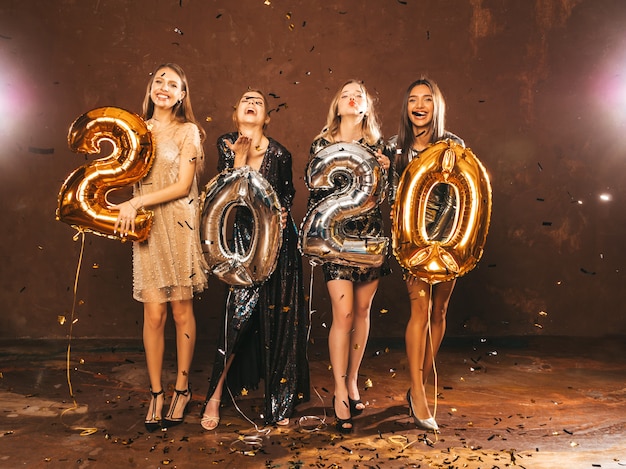 Niñas hermosas felices en elegantes vestidos de fiesta sexy con globos dorados y plateados 2020