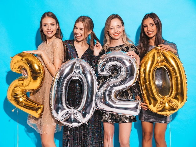 Niñas hermosas felices en elegantes vestidos de fiesta sexy con globos dorados y plateados 2020