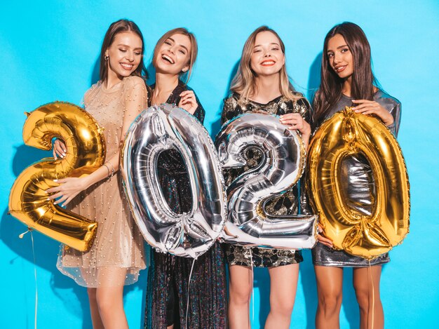 Niñas hermosas felices en elegantes vestidos de fiesta sexy con globos dorados y plateados 2020