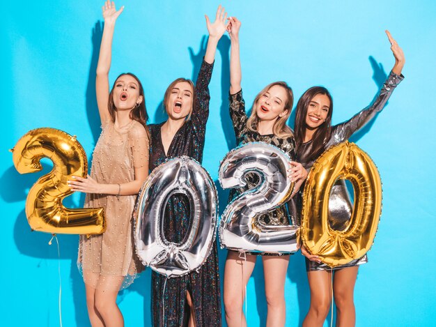 Niñas hermosas felices en elegantes vestidos de fiesta sexy con globos dorados y plateados 2020