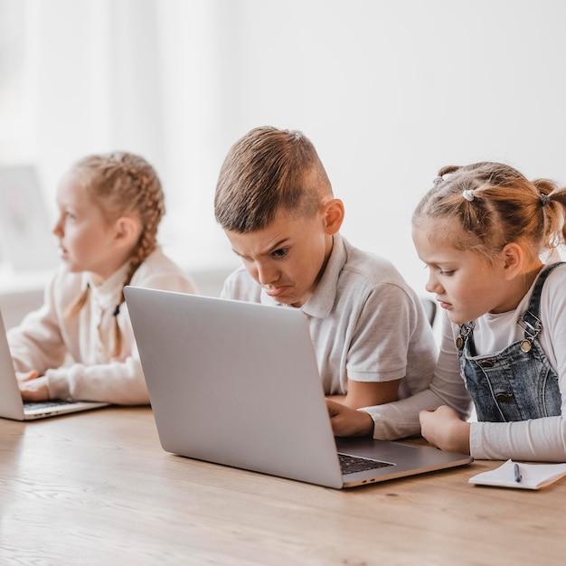 Niñas y niños usando computadoras portátiles en la escuela.