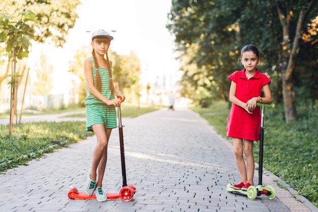 Niñas de pie con scooter en el pavimento