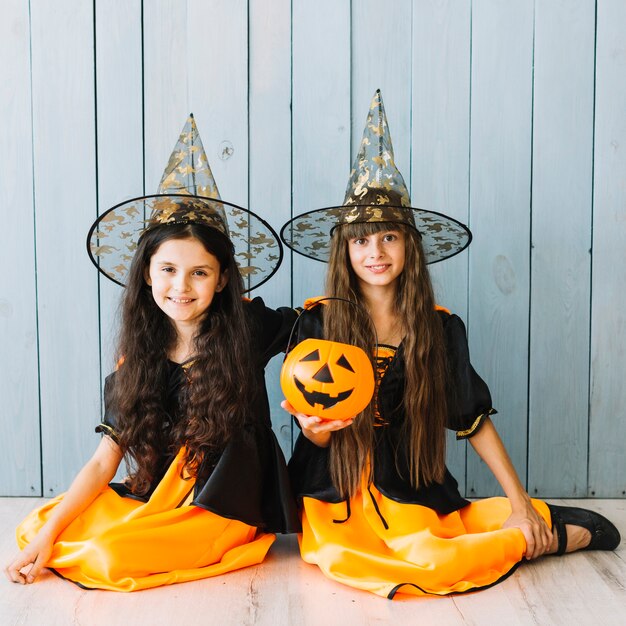 Niñas con sombreros puntiagudos sentados en el piso con el cubo de Halloween