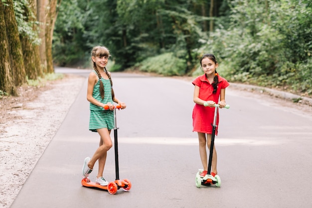 Niñas sonrientes que se colocan sobre la vespa del empuje en el camino