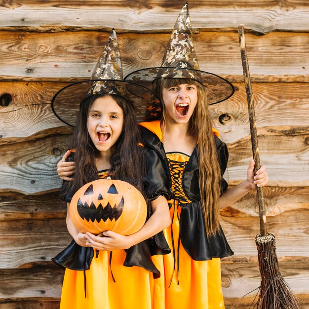 Niñas con trajes de bruja haciendo caras sosteniendo una escoba y calabaza