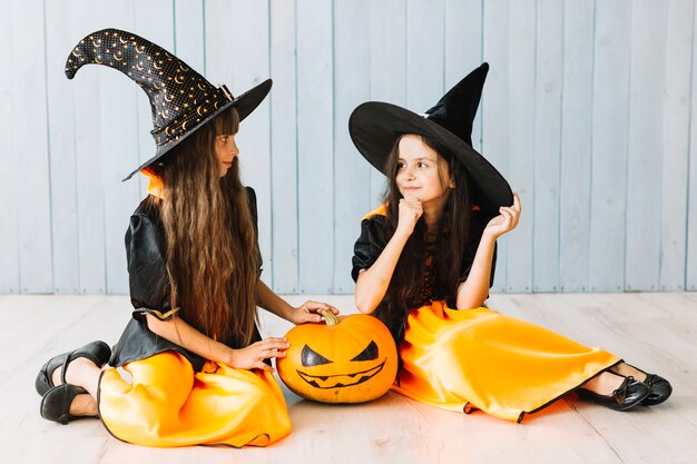 Niñas en trajes de bruja sentados en el piso con calabaza