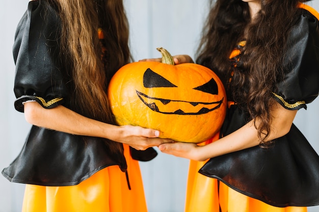 Niñas con trajes de bruja sosteniendo juntos calabaza de halloween