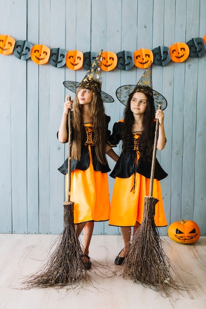 Foto gratuita niñas en trajes de brujas abrazándose y sosteniendo palos de escoba