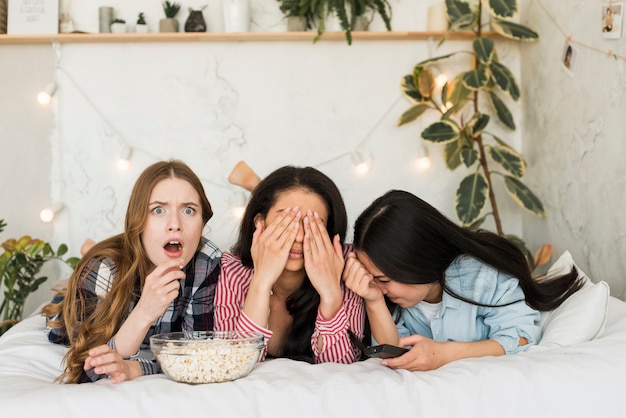 Niñas tumbadas en la cama y comiendo palomitas y divirtiéndose.